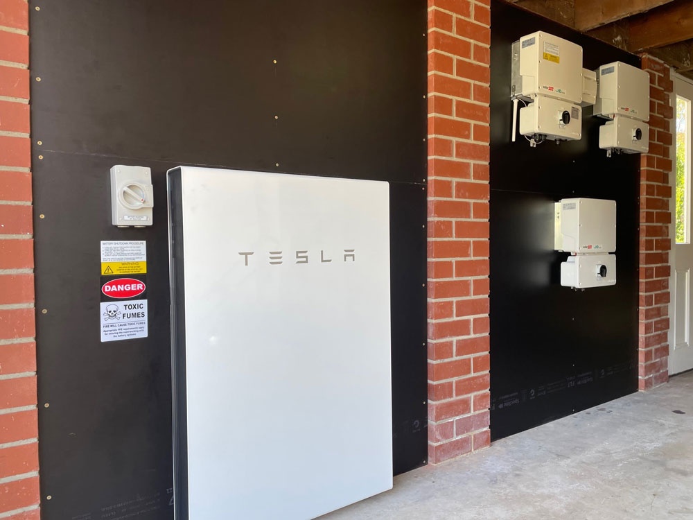Wall-mounted Tesla Powerwall battery and SolarEdge inverter equipment beside a brick wall